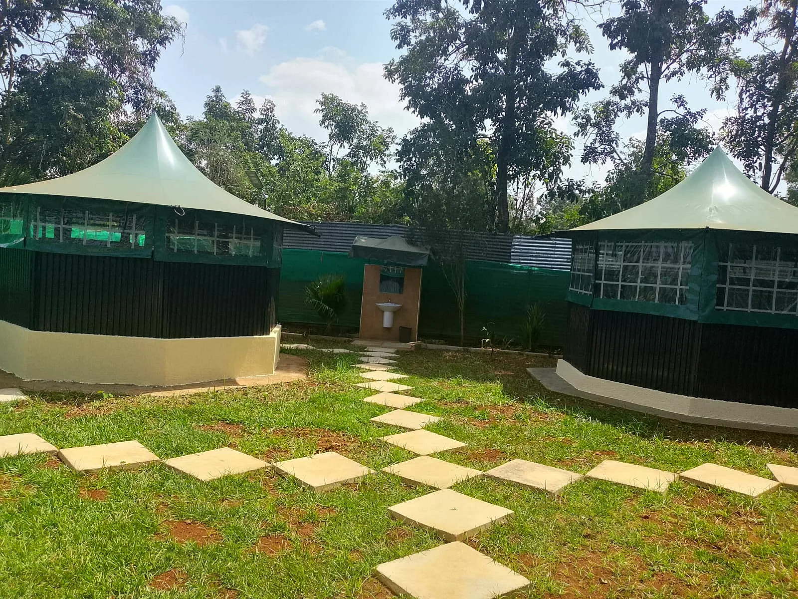 Two green garden gazebos connected by stepping stones across the lawn