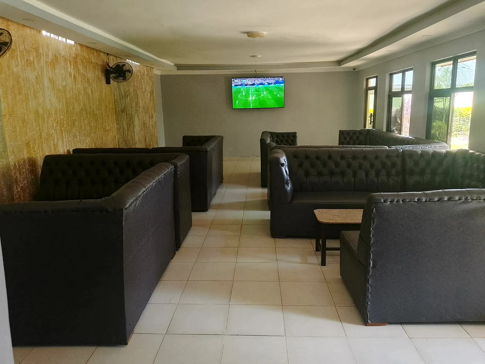 Spacious lounge with leather seating arranged around a wall-mounted TV showing football